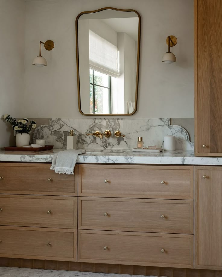 a bathroom vanity with marble counter top and wooden cabinetry, along with a large mirror above it