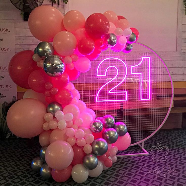 the number twenty one is surrounded by pink and silver balloons in front of a neon sign