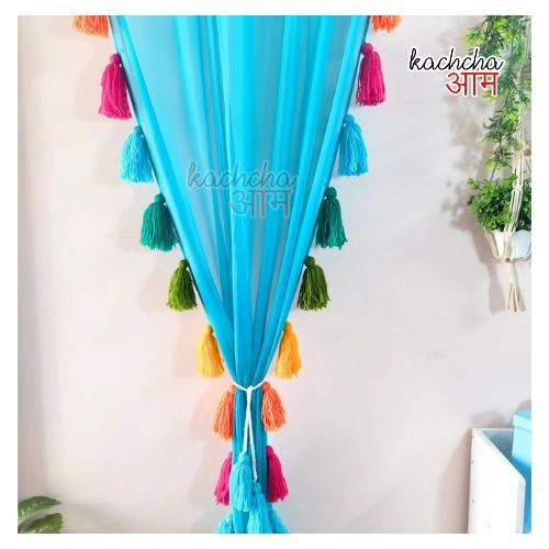 a blue curtain with colorful tassels hanging from it's side in front of a potted plant