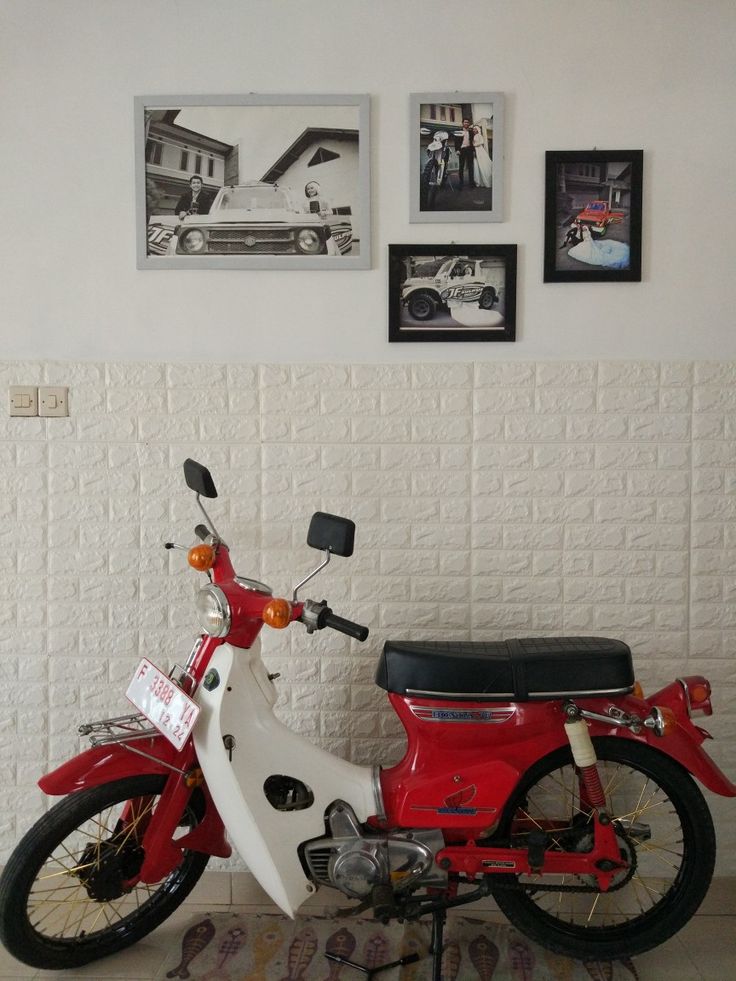 a red and white moped parked in front of a wall with pictures on it