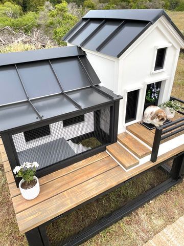 a dog house with a cat in it on top of a wooden platform next to grass and trees