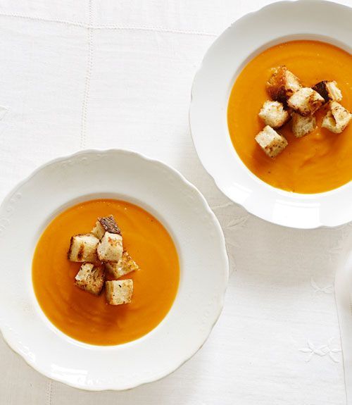 two white bowls filled with soup and croutons sitting on top of a table