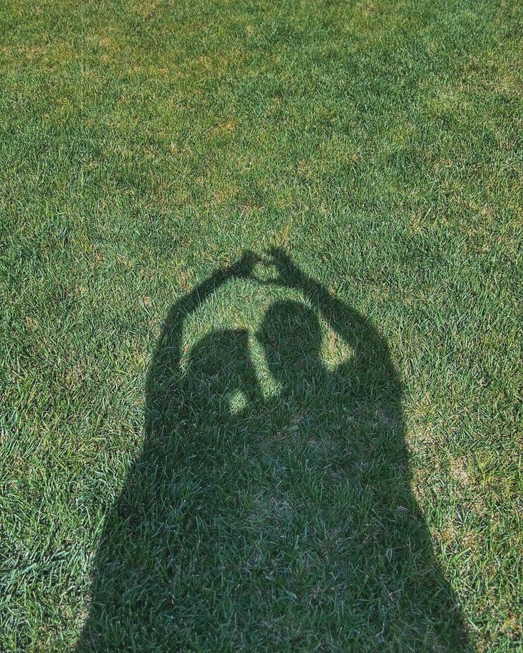 the shadow of a person holding a frisbee in their hand on some grass