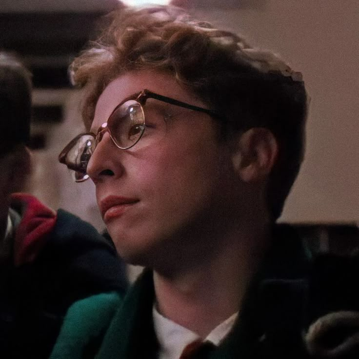 a young man wearing glasses looking off into the distance