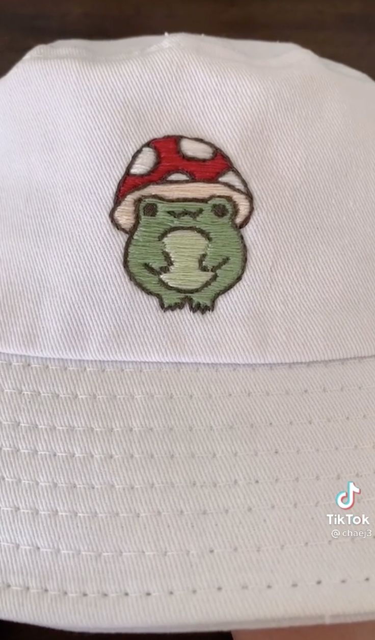 a white hat with a green frog wearing a mushroom on it