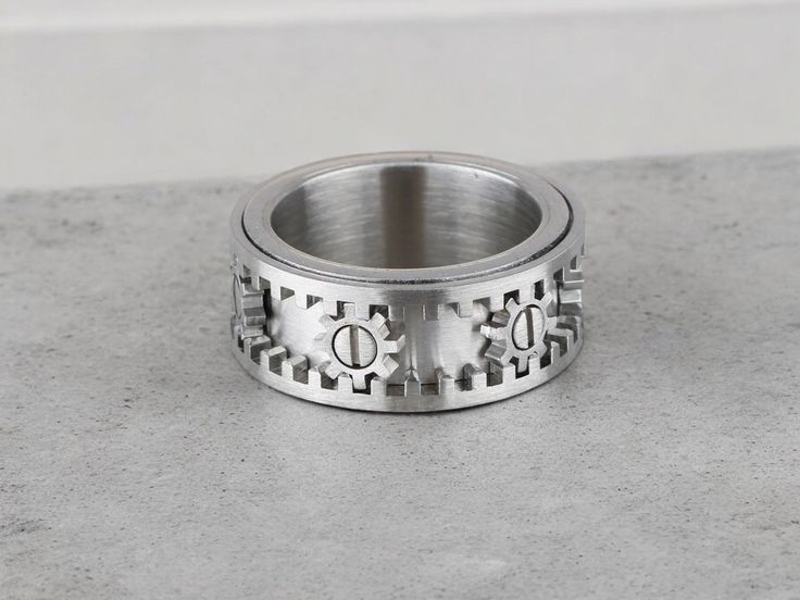 a stainless steel ring with an ornamental design on the outside and inside, sitting on a concrete surface