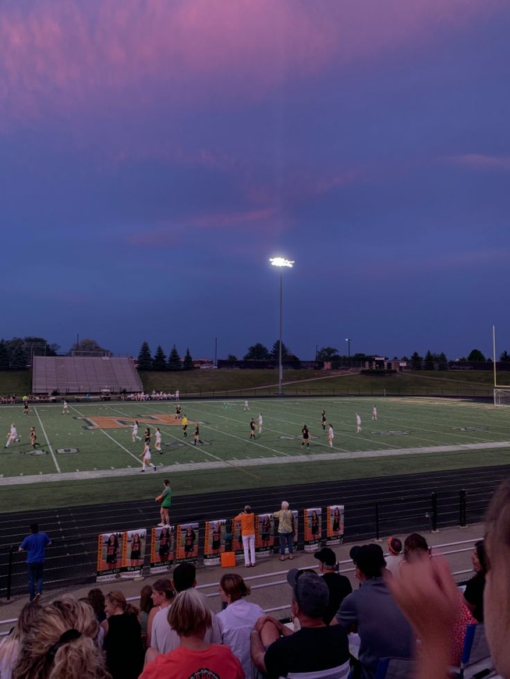 a group of people sitting on top of a field watching a soccer game at night