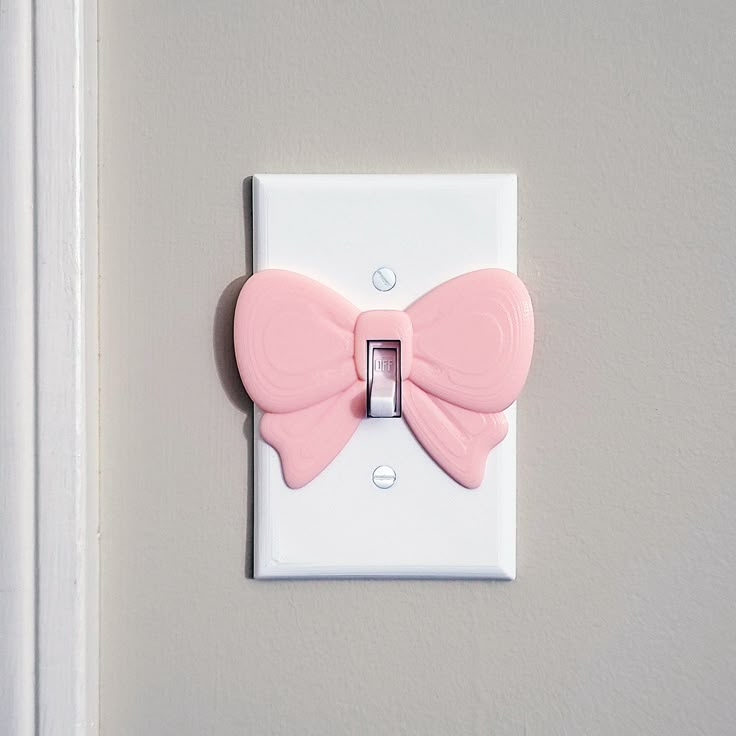 a light switch with a pink bow decoration on it's side and a white wall in the background