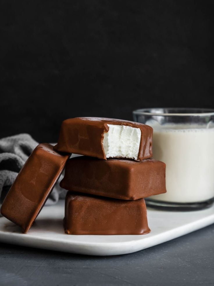 three pieces of chocolate covered marshmallows on a plate next to a glass of milk