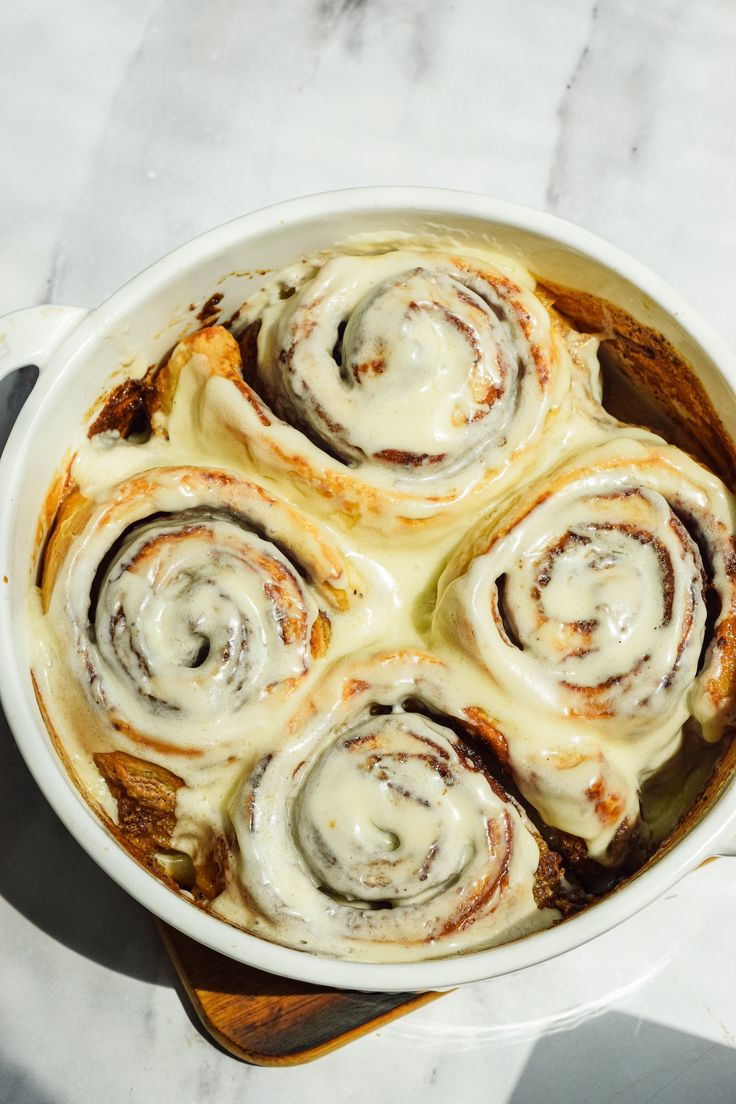 a pan filled with cinnamon rolls on top of a wooden cutting board