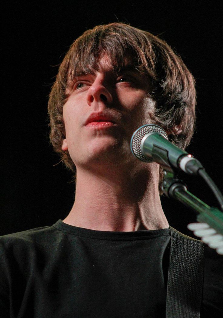 a young man holding a guitar in front of a microphone and looking up at the sky