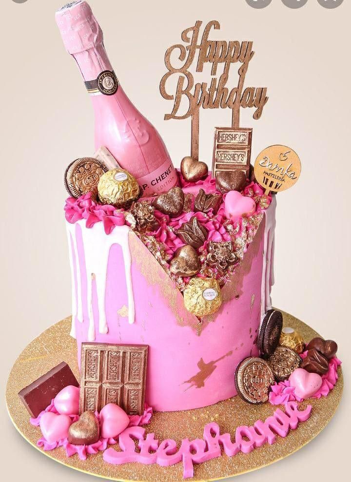 a pink birthday cake decorated with chocolates, candies and a bottle of champagne