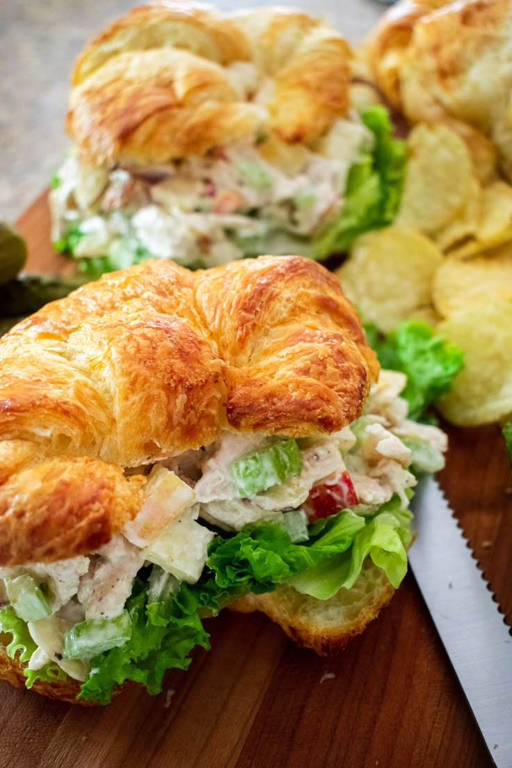 a croissant sandwich with lettuce and chicken on it next to potato chips