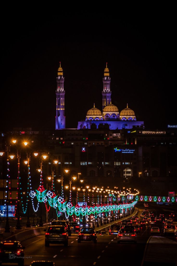 cars driving down a busy city street with christmas lights on the trees and buildings in the background