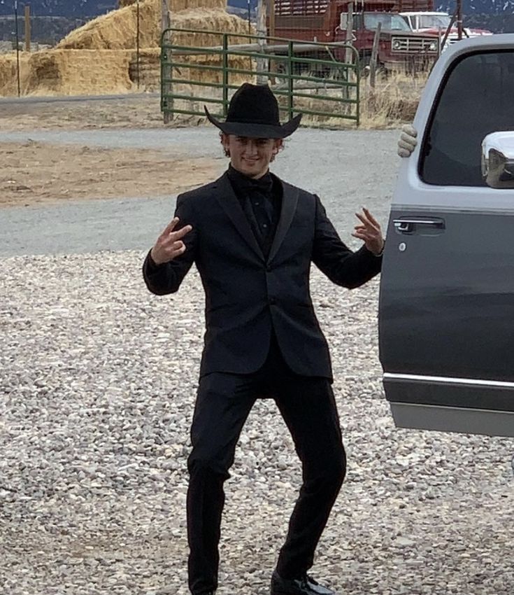 a man in a black suit and hat standing next to a silver truck