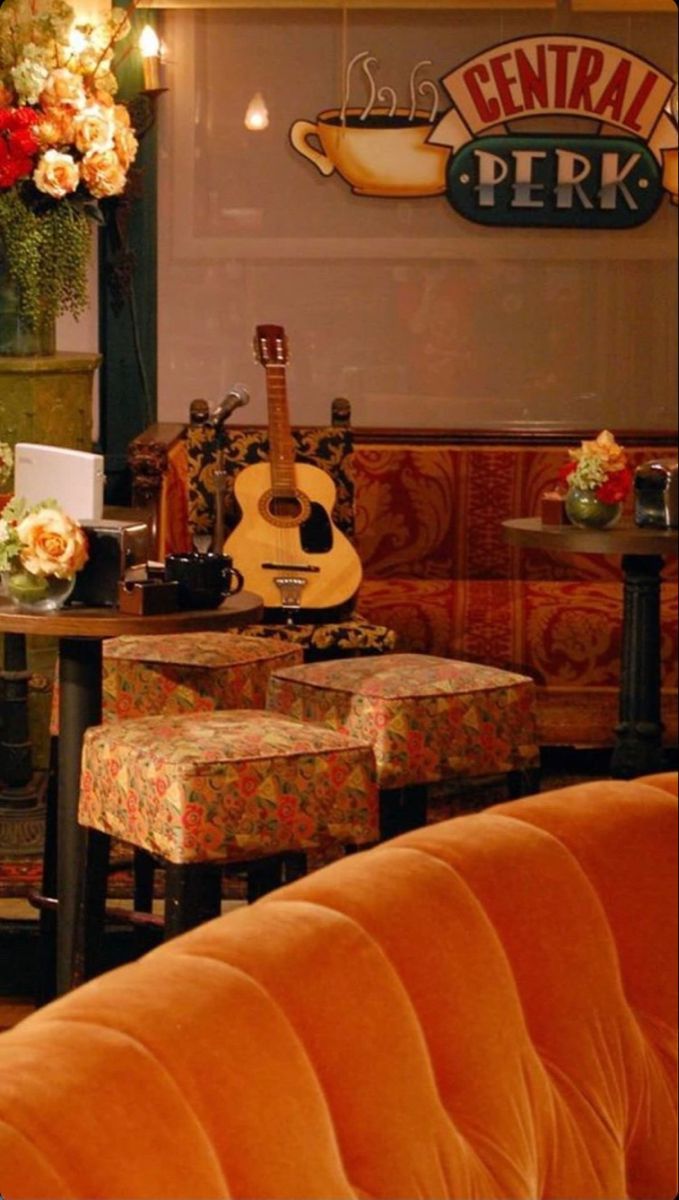 an orange couch sitting next to a table with a guitar on top of it in front of a sign that says central perk