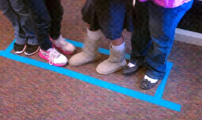 three people standing in front of a blue line on the floor with their feet up