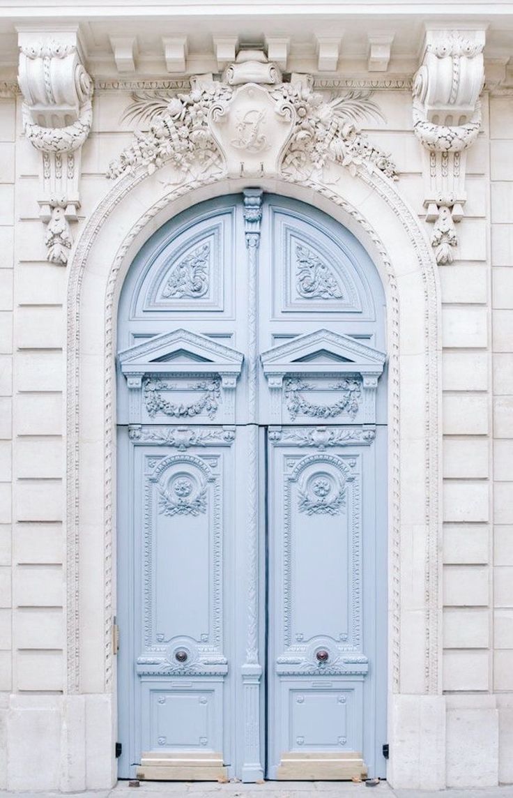 two blue doors are open in front of a white building with ornate carvings on it