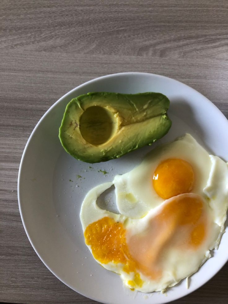 an avocado and two eggs on a white plate