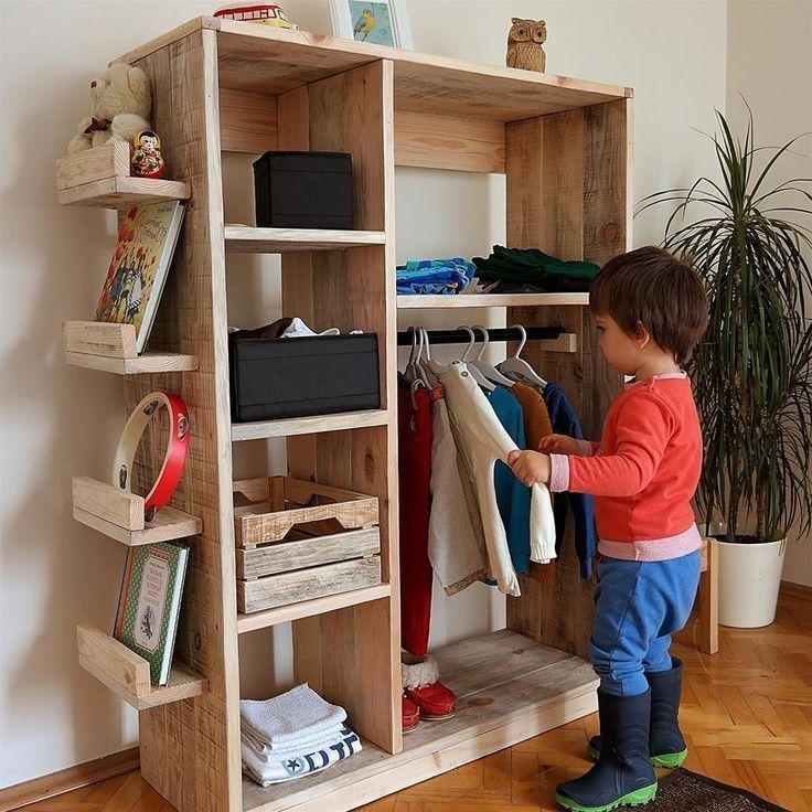 a little boy that is standing in front of a shelf with some clothes on it