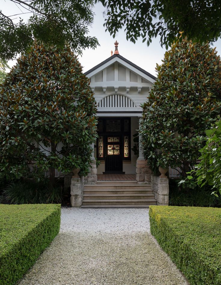 the entrance to a white house surrounded by hedges