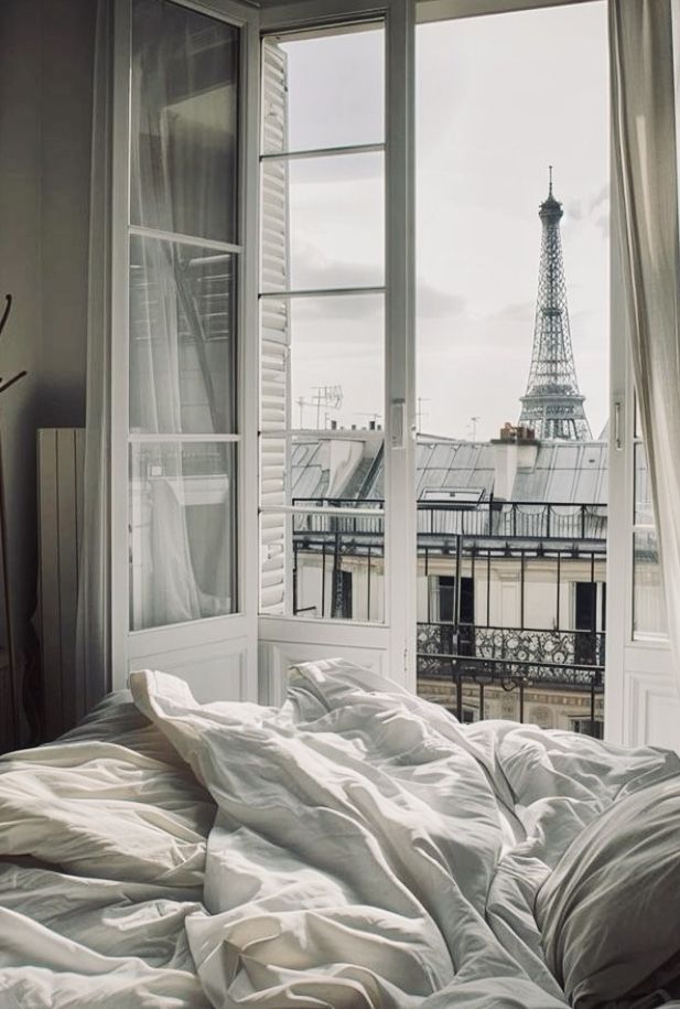 an unmade bed in front of a window overlooking the eiffel tower