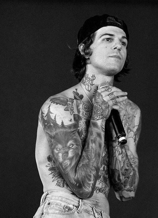 a man with tattoos on his chest holding a microphone and looking up at the sky