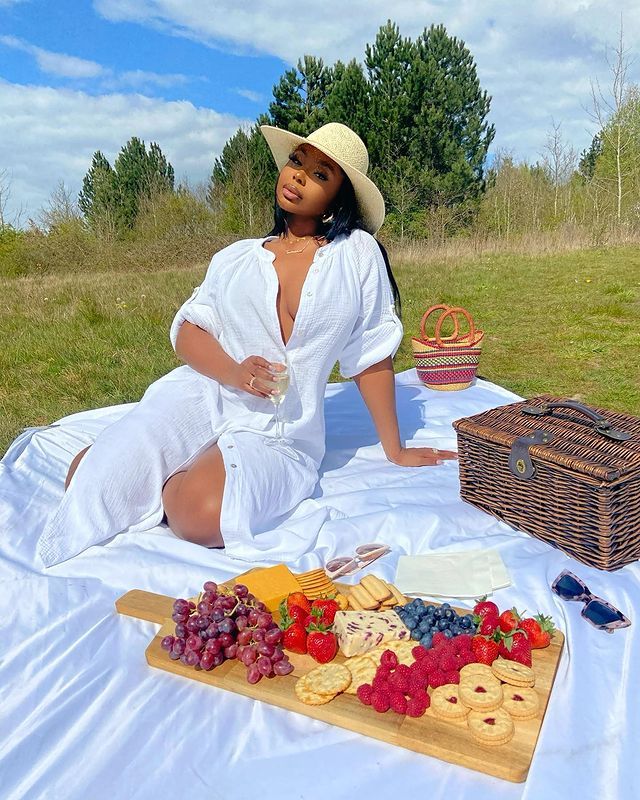 a woman in a white dress and straw hat sitting on a blanket with food items