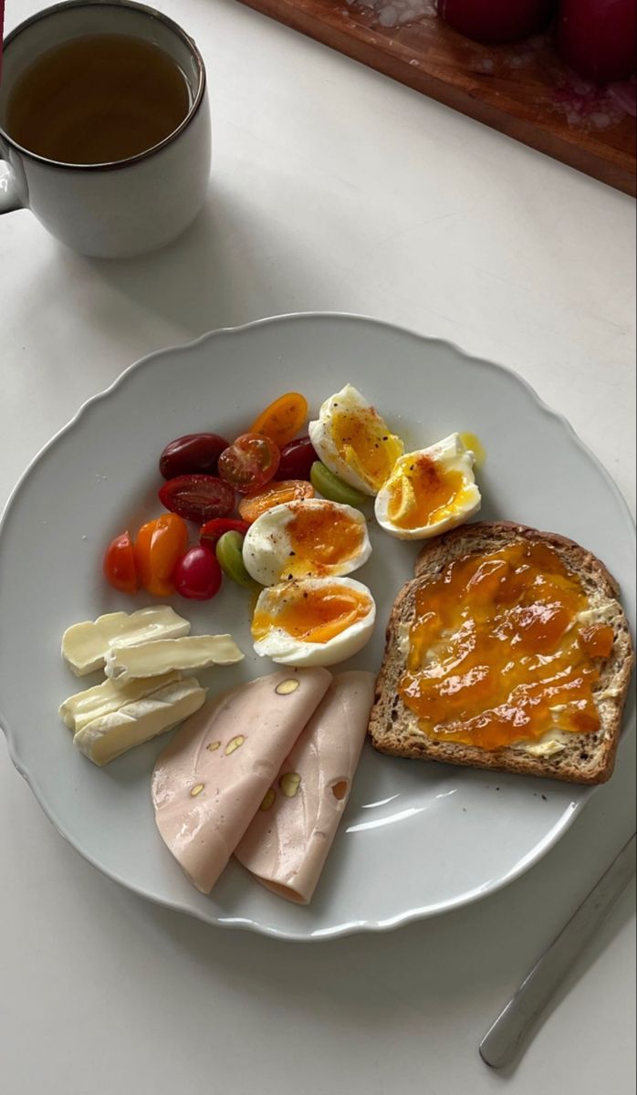 a white plate topped with eggs, meat and fruit next to a cup of coffee