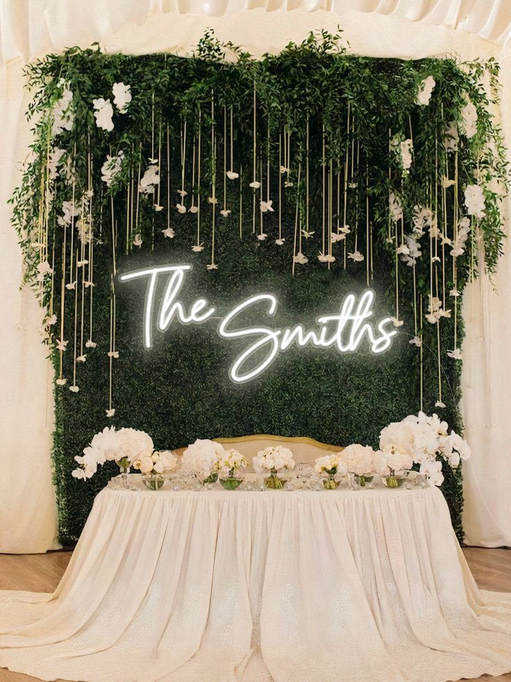 a table with white flowers and greenery on it, next to a green wall