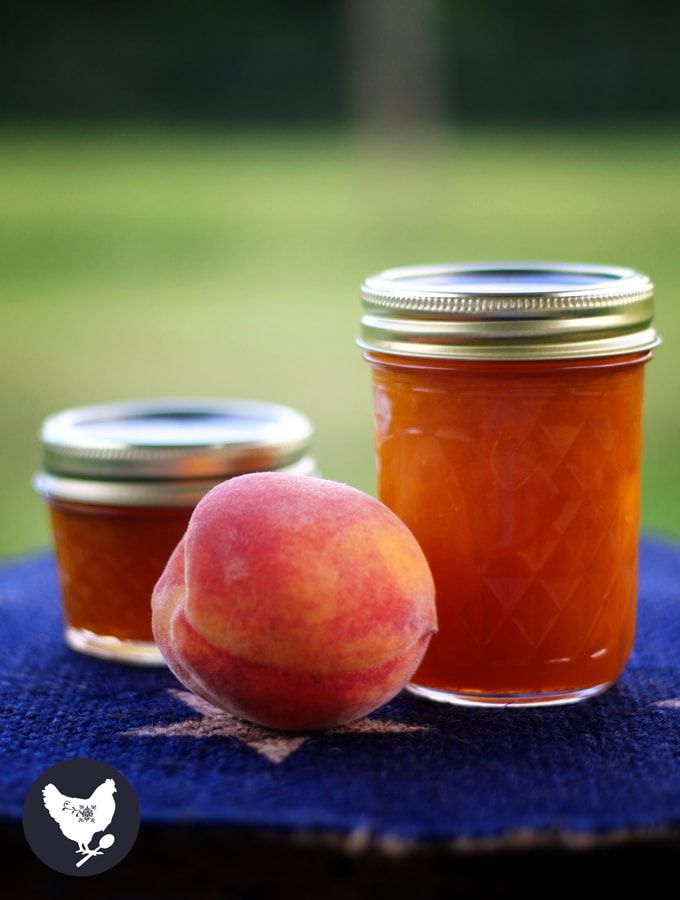 two jars filled with peach jam sitting on top of a blue cloth next to an apple