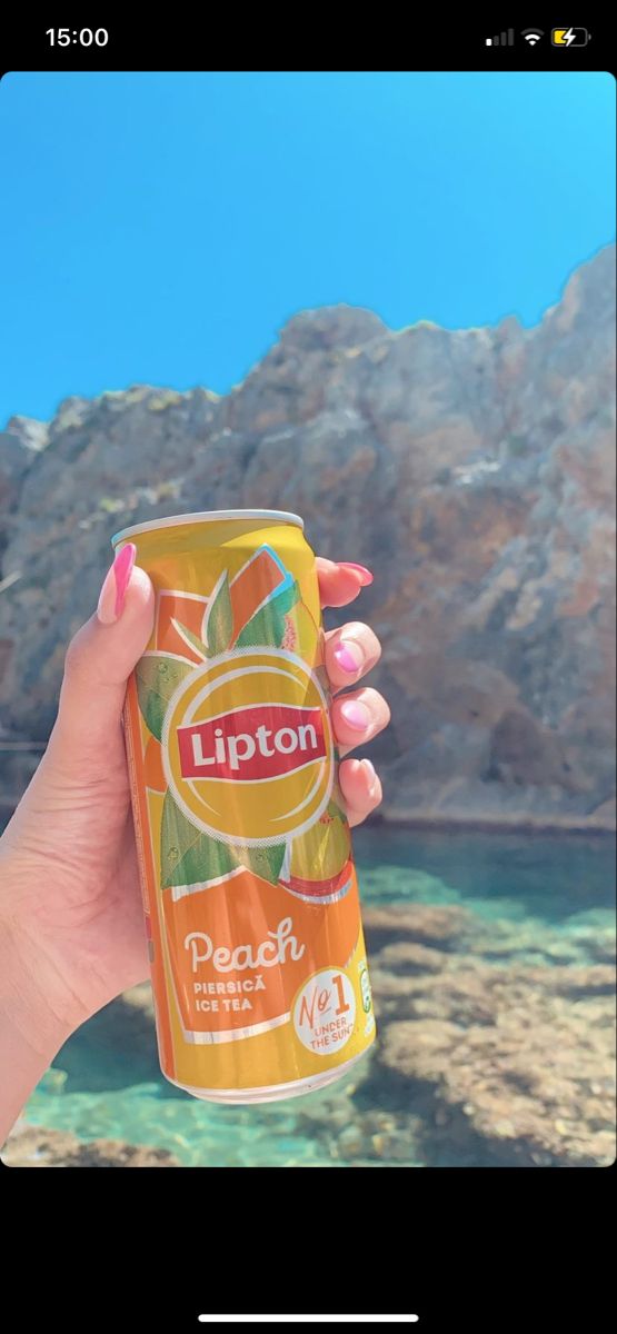 a woman holding up a can of lipton peach lemonade in front of mountains