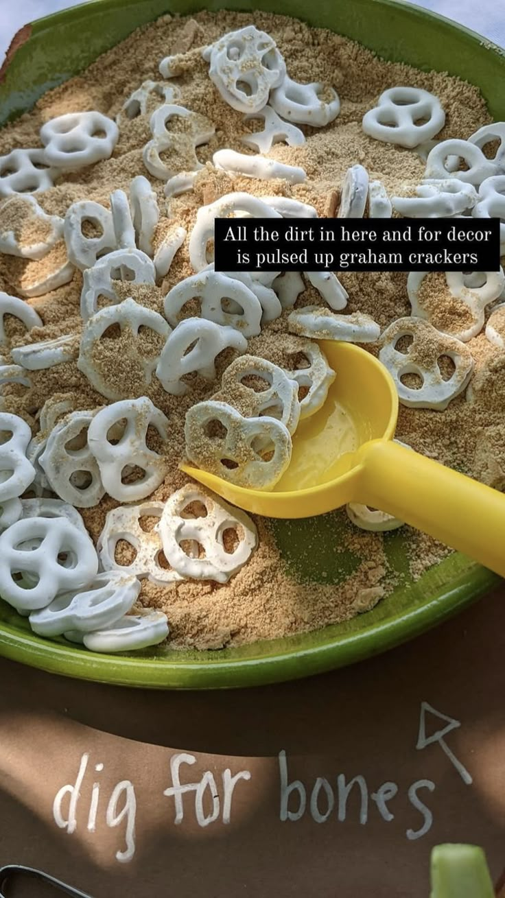 a green bowl filled with lots of white pretzels next to a sign that says dig for bones