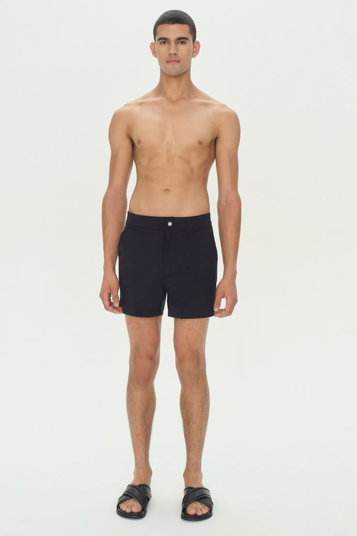 a man standing in front of a white background wearing black swim trunks and flip flops