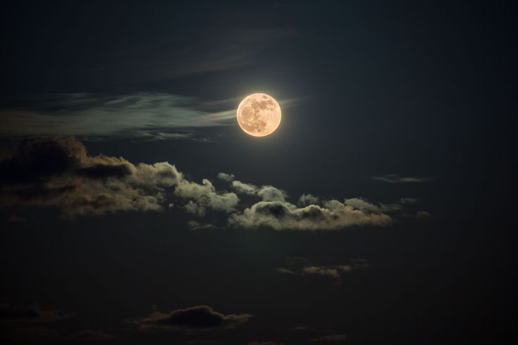 the full moon is shining brightly in the night sky with clouds and dark blue skies