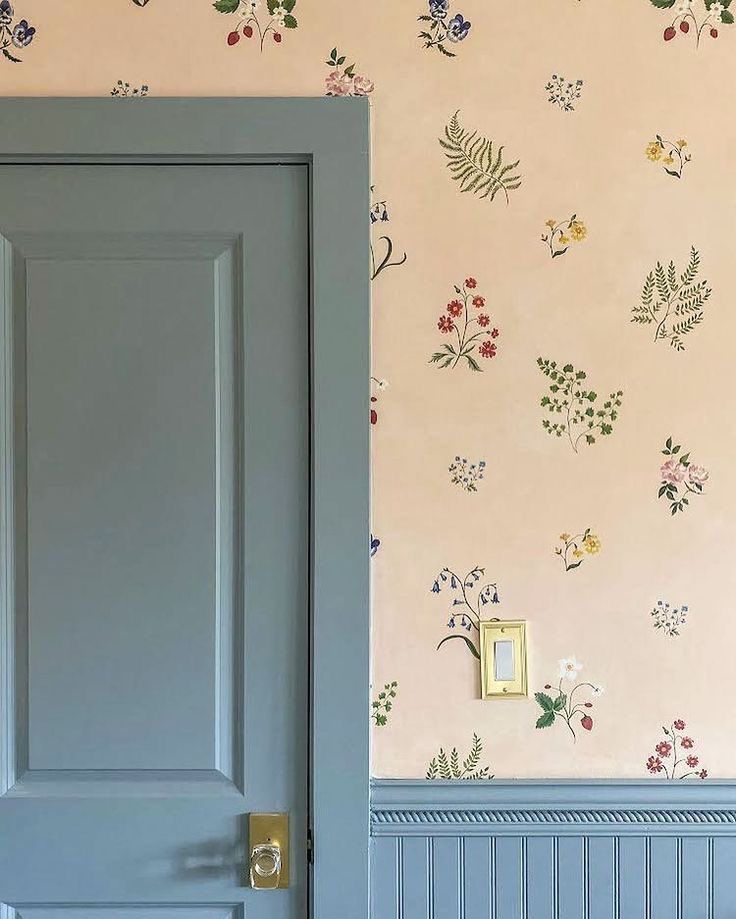 an open door in front of a floral wallpapered room with blue walls and wooden floors