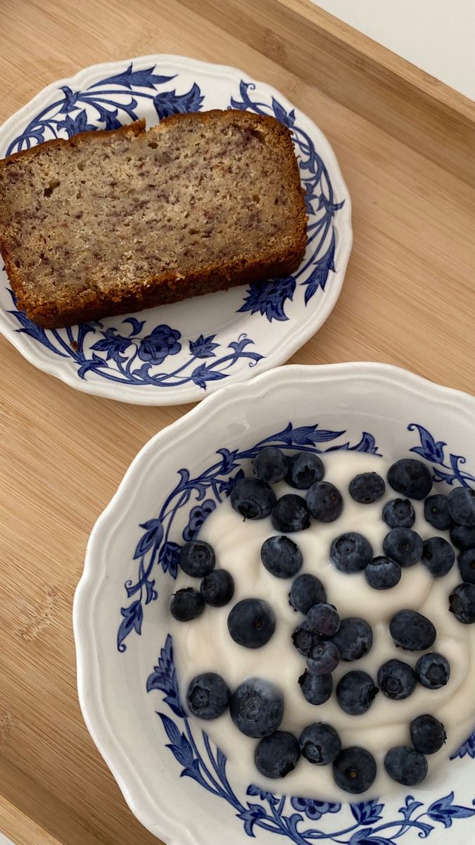 two plates with blueberries and yogurt on them next to a loaf of bread