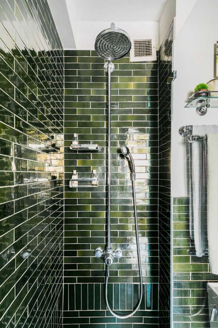 a bathroom with green tiles and a shower head in the corner, along with a sink