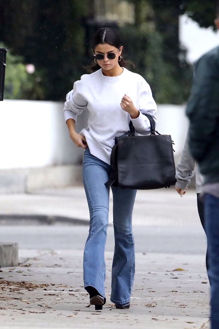 a woman walking down the street carrying a black handbag in her right hand and another man behind her