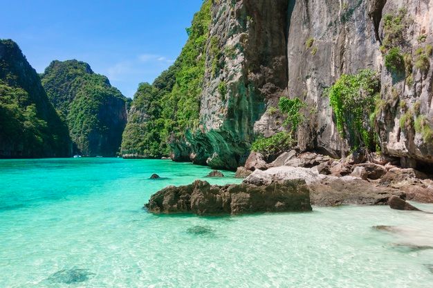 the water is crystal blue and clear in this tropical beach scene with rocks, green trees and cliffs