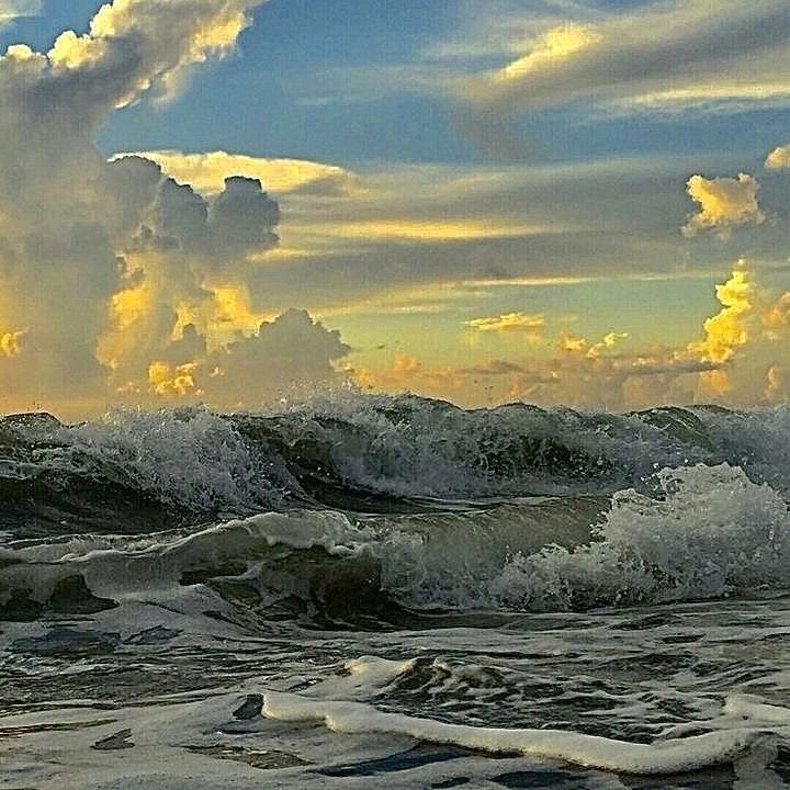 the sun is setting over the ocean with waves crashing on shore and clouds in the sky