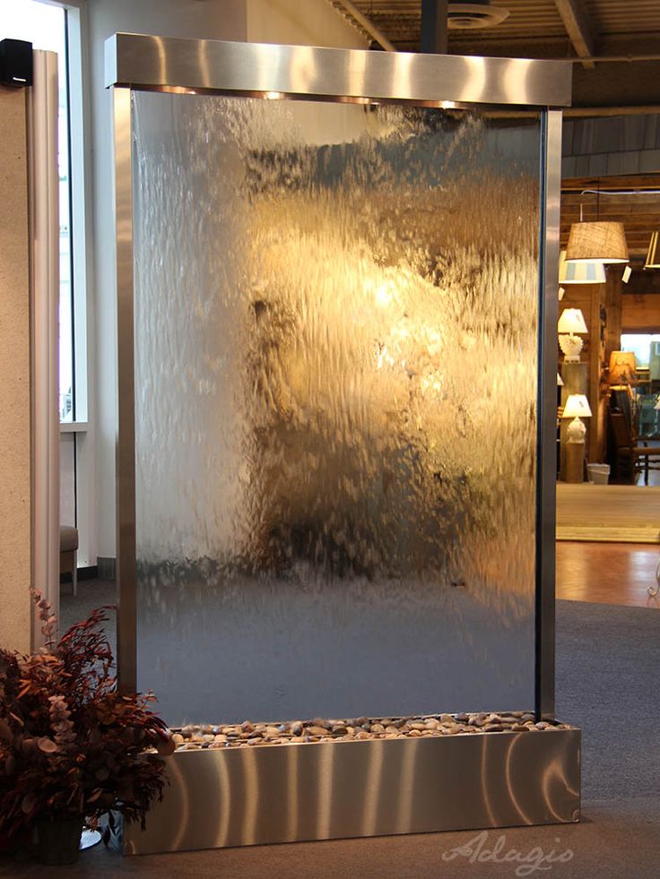 a water fountain in the middle of a building with lights on behind it and plants next to it