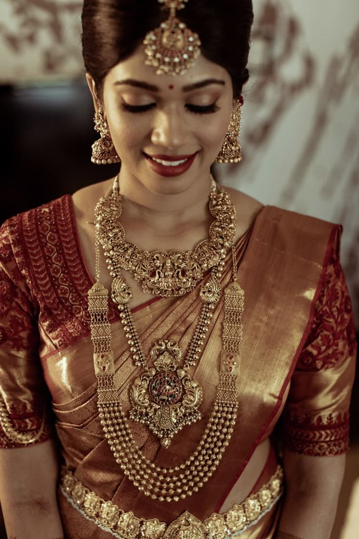 a woman in a red and gold sari with jewelry on her neck, smiling at the camera