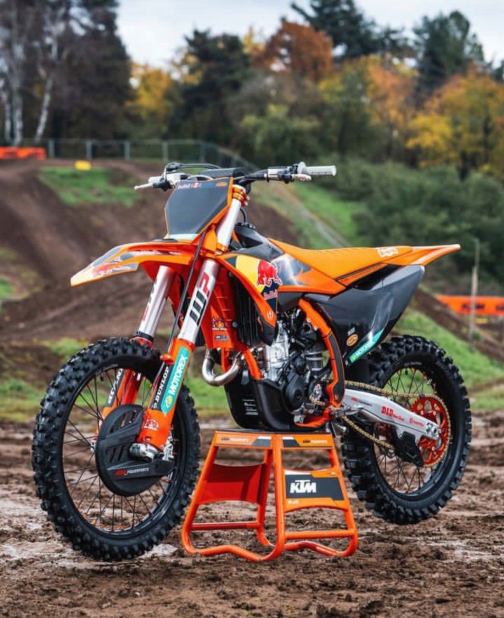 an orange dirt bike parked on top of a small stand in the middle of a muddy field