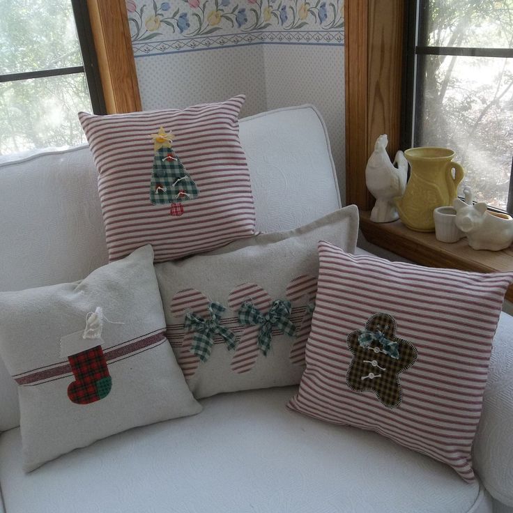 four christmas pillows on a white couch in front of a window with coffee pot and mug