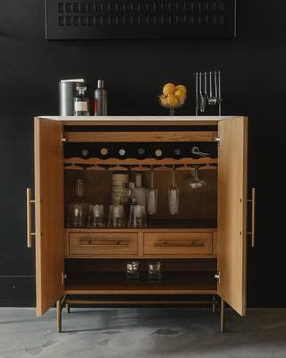 a wooden cabinet with wine glasses and bottles on it in front of a black wall