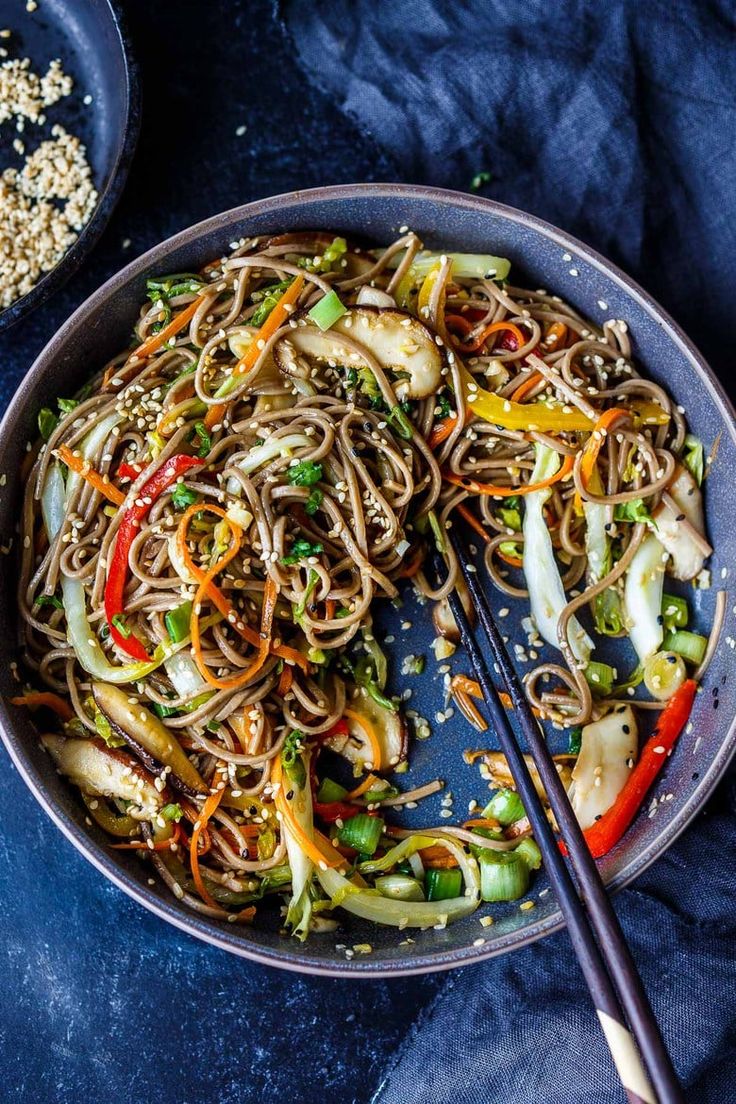 a bowl filled with noodles and vegetables on top of a blue cloth next to chopsticks