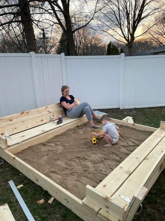 two children playing in an outdoor sandbox made out of pallets and wooden boards