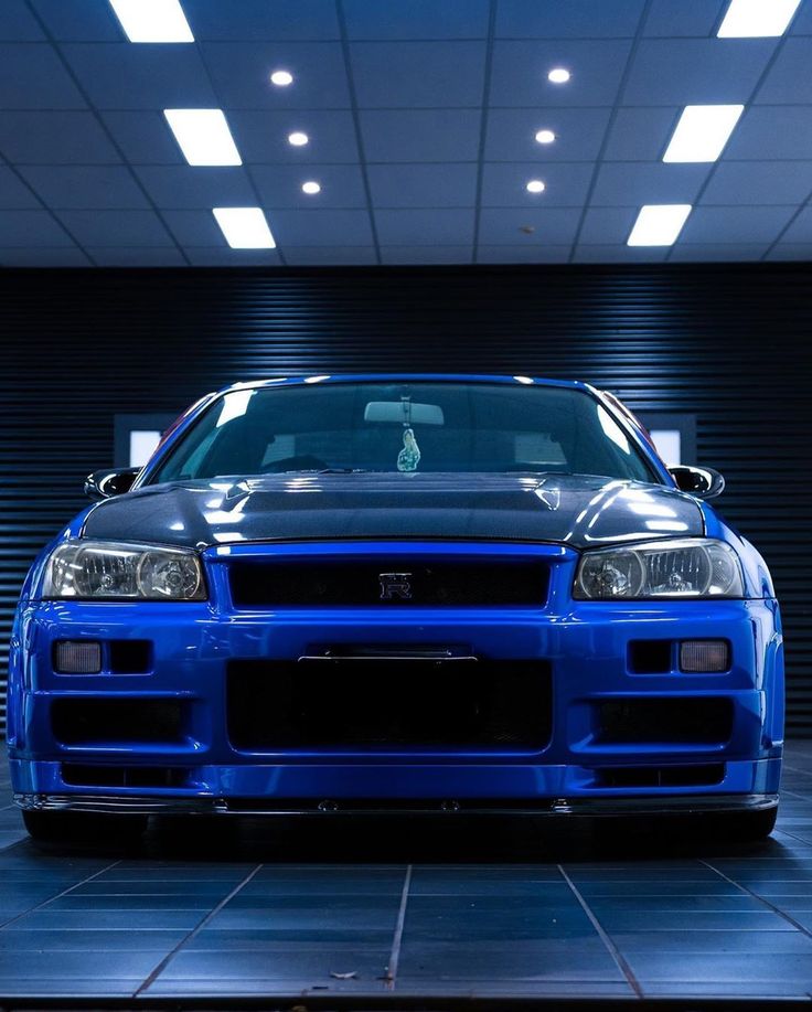 a blue car parked in front of a garage door with its hood up and lights on