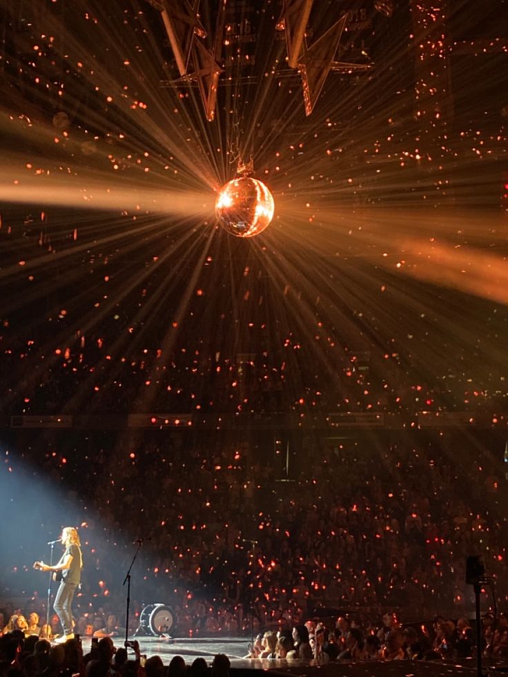 a person on stage with lights and confetti falling from the ceiling behind them